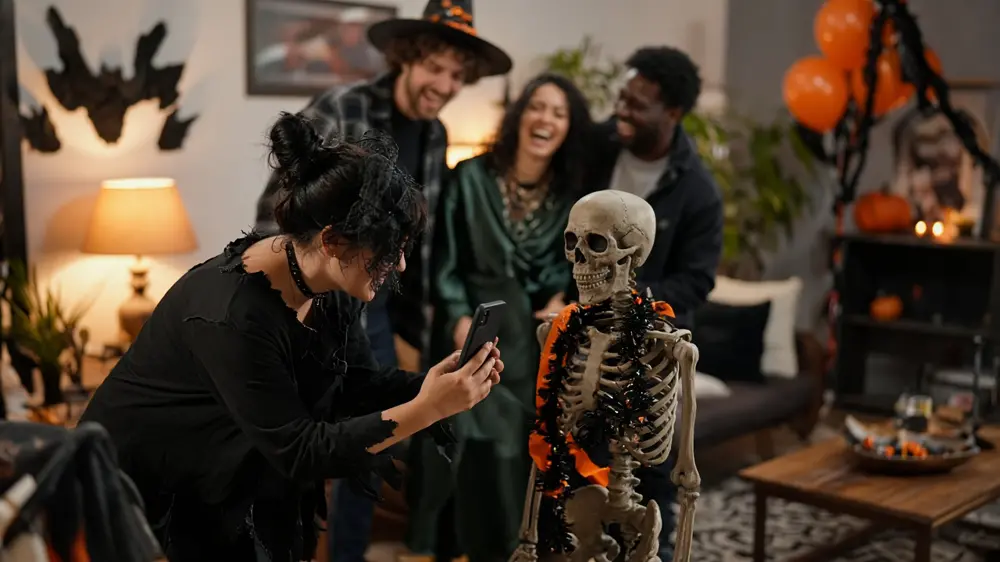 Guests at a Halloween party photographing a skeleton decoration on a phone